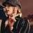 Pixelated anime-style character with blonde hair and dark clothing, wearing a cap, with orange text partially visible on the right side.
