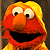 Pixelated static image of a red muppet character with yellow hair, large white eyes with black pupils, and an open mouth showing dark interior.