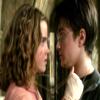 Two people face each other closely in a static image with blurred background, one in pink top and the other in dark jacket with white collar.