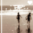 Two dark silhouettes walk side-by-side on a beach toward the water, with white wave patterns and a heart symbol above them.