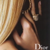 A close-up of a person with long blonde hair wearing a gold necklace and large gold earrings, with the word 'Dior' visible in white text at the bottom right.