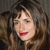 A pixelated close-up of a person with brown hair, red lips, and a neutral expression against a dark background.