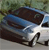 Static pixelated image of a dark blue car with white accents on a light gray surface, set against a blurred green background.