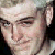 Pixelated close-up of a person's face with light skin tone, visible eyes, nose, mouth, and ear, set against a dark background with light-colored hair.