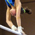 Static image of a gymnast performing on a balance beam with visible legs, feet, and partial torso in blue leotard against dark background.