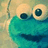 Pixelated image of a blue puppet-like character with large eyes and a wide mouth, next to green text reading "Musice is lifee" on a white background.