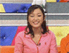 A person in a pink zip-up jacket with a small red logo on the chest, seated against a colorful background with blue, yellow, and orange sections.