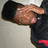 Pixelated image of a person in dark clothing with one hand raised near their face, set against a light background.