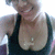 A person in a black tank top with a small pendant necklace smiles broadly, showing teeth, in a bright indoor setting.