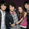 Four people pose closely together against a dark purple background, with two individuals in the center embracing.