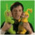 Two side-by-side animated frames show a person in yellow and black clothing holding green and yellow objects against a solid green background, then turning to face right with a thumbs-up gesture.
