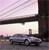 Static image of a silver sedan on a road beneath a bridge with a pinkish sky background.