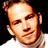 Pixelated static image of a person's face with light skin tone, brown hair styled in a bun or topknot, wearing a white shirt against black background.