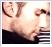 A pixelated static image shows a person with light skin and dark hair wearing a black top, holding an object near their face.