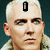 A pixelated image of a person with short light hair, wearing a light-colored jacket, with a black rectangular icon on the forehead in the first frame and a black circular icon with a white symbol in the second frame.