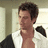 Pixelated image of a person with short dark hair wearing a white shirt with dark shoulder patches, standing against a light background with vertical elements.