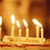 A golden candelabra with six lit candles on a flat base, set against a warm brown gradient background.