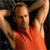 A person in an orange sleeveless top with arms raised behind their head, set against a dark background with light-colored vertical elements.