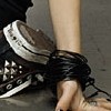 A close-up of a person's lower leg and foot wearing a black and white sneaker with a white sole and black laces, bound by a black strap.