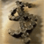 A pixelated image of a dark, abstract shape resembling a stylized animal or creature against a light brown background with subtle gradient.