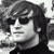Black-and-white pixelated image of a person with dark hair and sunglasses, wearing a dark top against a blurred background.