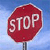 Red octagonal sign with white 'STOP' text on a blue sky background, mounted on a dark pole.