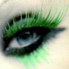 Close-up of a stylized human eye with exaggerated green eyelashes and dark eyeshadow on a light background.