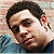 Pixelated static image of a person's face with dark hair and light skin, wearing a blue garment against a blurred background.