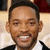 Pixelated close-up of a smiling person with short dark hair wearing a dark suit jacket over a white shirt, set against a light background with dark and red elements.