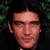 Pixelated static image of a person's face with dark hair and green foliage background, rendered in low-resolution 256x256 pixels.