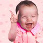Static image of a baby in pink clothing making a peace sign against a light pink polka-dot background.