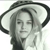A grayscale pixelated image of a person wearing a wide-brimmed hat with a dark band, long hair, and a light-colored garment, set against a plain background.