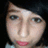 Pixelated close-up of a person's face with light skin, blue eyes, and pink lips against a dark background.