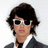 Pixelated image of a person with dark hair wearing white-framed sunglasses, a white shirt, and dark jacket against light background.