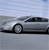 Pixelated static image of a silver convertible car with a black soft top, viewed from the side against a light blue sky and gray ground.