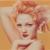 Pixelated image of a person with light brown hair styled up, wearing a white top, against a solid orange background.