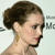 Pixelated profile of a person with brown hair in a bun, wearing a gold earring and dark choker, against a light background with partial text.