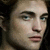 Static pixelated image of a person's face with light skin tone, dark eyebrows, blue eyes, and closed lips against a dark background.