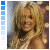 A woman with long blonde hair and a white strapless dress smiles at the camera against a blurred background of warm lights.