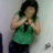 Pixelated image of a person with dark hair wearing a green sleeveless top and dark pants, hands raised near chest in a gesture.
