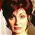 Pixelated close-up of a person with dark curly hair, light skin tone, and visible facial features including eyes, nose, mouth, and ear.