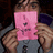 A person holds a pink square card with dark pixelated symbols against a blurred background.