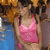 A woman in a pink tank top and blue jeans stands against a blurred background with brown and blue tones.