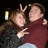 Two people in close embrace, one making a peace sign with both hands against dark background.
