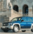 Pixelated image of a blue and white vehicle with dark windows and wheels, positioned on a light-colored road against a blurred background.