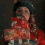 A person in a red floral dress and dark hat appears in four showing slight head and hand movements against a dark background