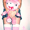 A person holds a pink plush toy with red dripping mouth, wearing checkered shorts and striped socks.