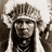 Black-and-white photograph of a person wearing a feathered headdress and beaded necklaces on a red background with pixelated text.