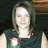 A pixelated image of a person with shoulder-length hair wearing a dark sleeveless top and a red-and-white flower pin, set against a dark background.