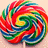 A circular, pixelated lollipop with swirling red, green, blue, yellow, and white segments on a light beige background.